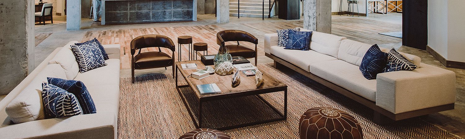 Living space with wicker rug, wooden coffee table & beige sofas with blue throw pillows