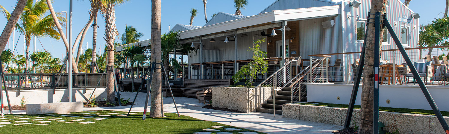 Barrell House exterior with lawn and palm trees and stairs leading to tables and chairs