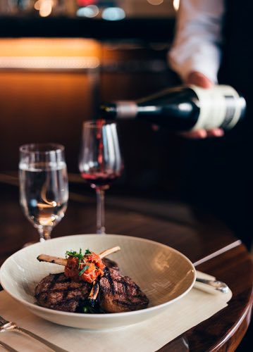 Plate with lamb chops next to wine glasses