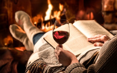 woman reading by the fireplace with a glass of wine