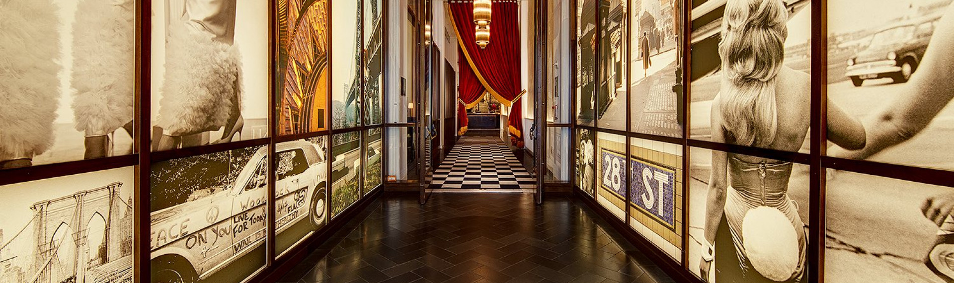 a hallway with large murals on the walls and double glass doors leading to a black and white checkered floor with two large red curtains gathered at the side