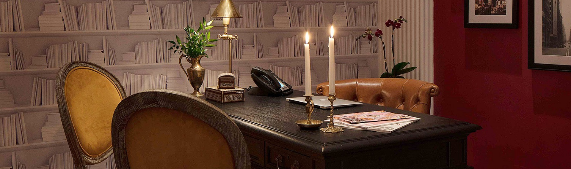 office desk with brown chairs, two lit candlesticks, and white bookcase wallpaper