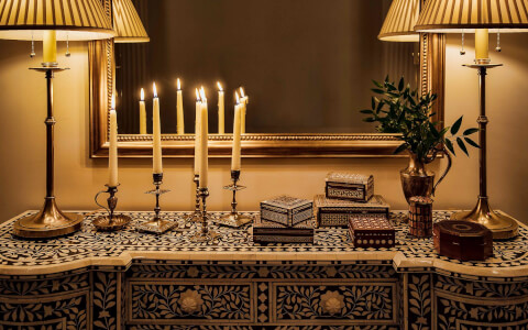 patterned entry way table with two laps and several lit candlesticks in front of a mirror