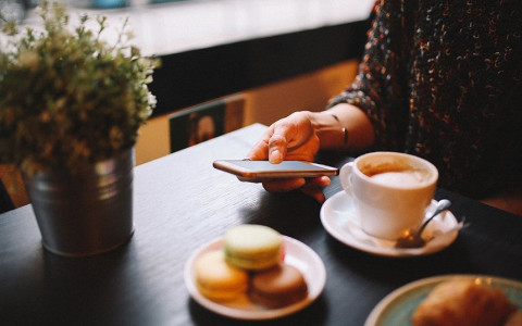 Close up of a woman on her phone sitting at a table with a cup of coffee and a plate of macaroons