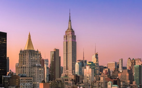 the empire state building and other buildings with a purple and pink sky in the background