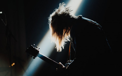 A dark image of a man playing the guitar with the spotlight shining behind him