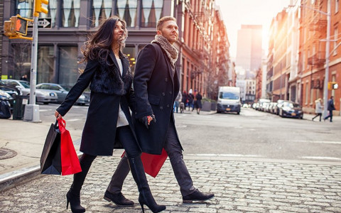 A man and a woman are holding hands as they cross the street holding their shopping bags
