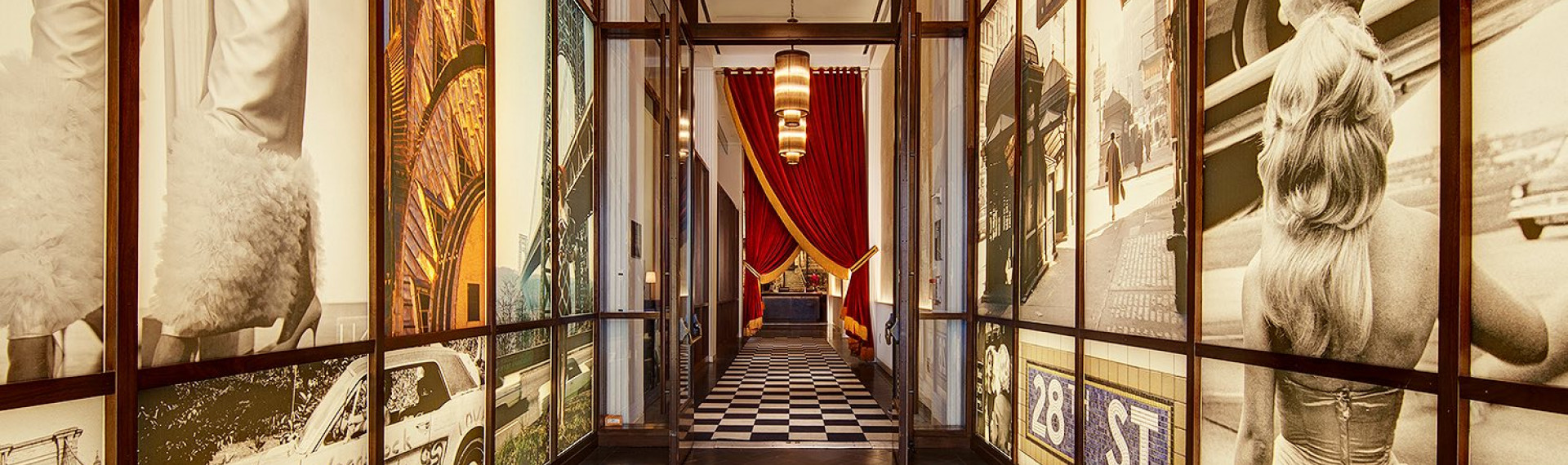 a hallway with large murals on the walls and double glass doors leading to a black and white checkered floor with two large red curtains gathered at the side