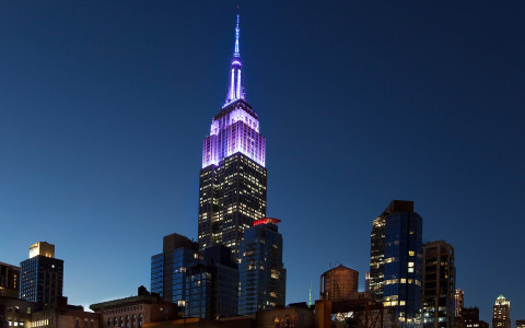 the top of the empire state building lit up purple at night