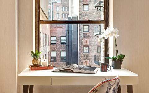a desk and chair in front of a window looking out to a brick building