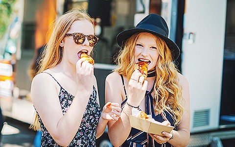 two teenagers eating food from a street vendor