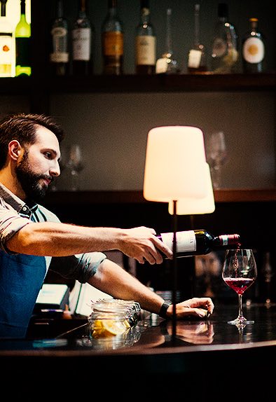 a bartender pouring a glass of red wine at the bar