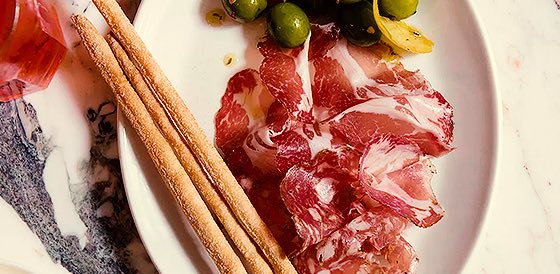 prosciutto, olives, and cracker sticks on a plate