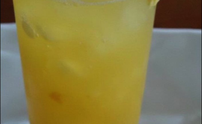 Fruity yellow mango cocktail in tall glass with orange slice