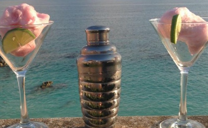 Two martini glasses garnished with pink cotton candy and a drink shaker is in between the two glasses