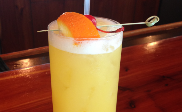 Fruity yellow mango cocktail in tall glass with orange slice