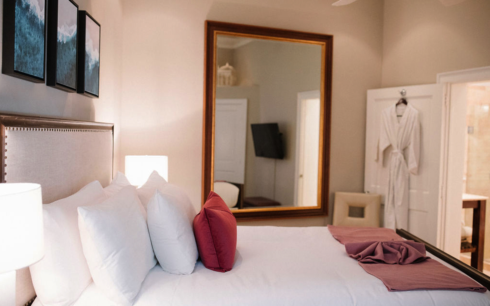 side view of a double bed with a wall mirror and a rob hanging in a door