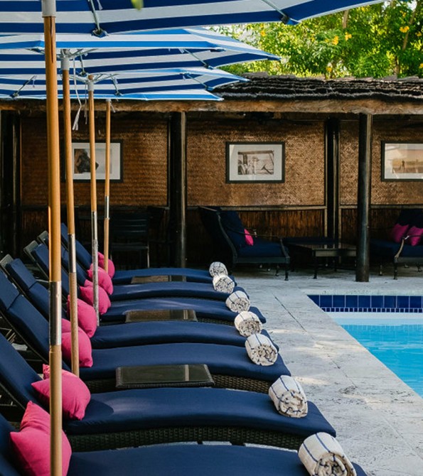 Dark chaise lounges with blue umbrellas next to swimming pool