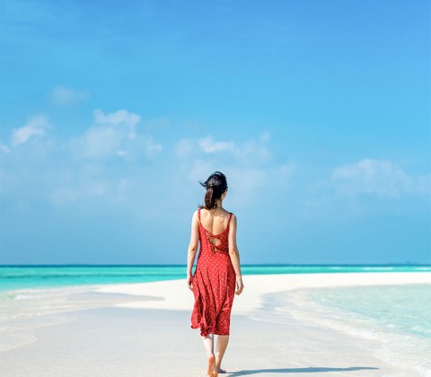 Back of a woman on a red dress walking on the beach