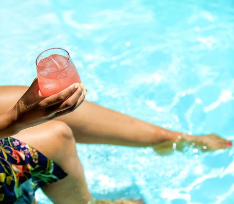 A woman holding a glass with a tropical beverage next to the pool