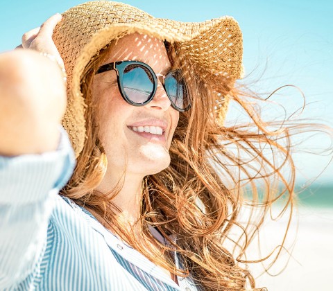 Happy redhead woman smiling and wearing a beach hat and sunglasses