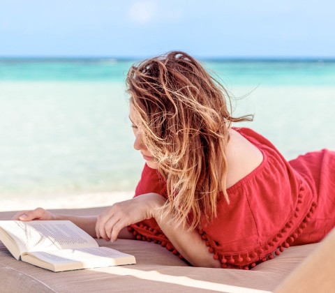Woman on a red dress reading by the beach