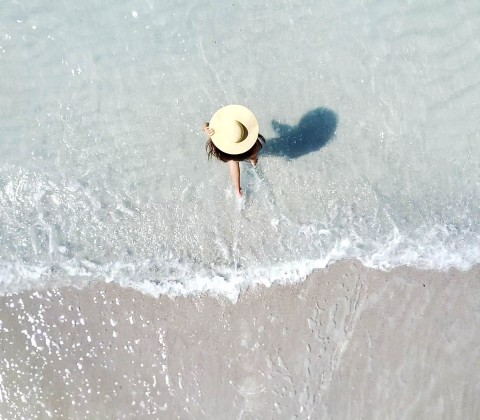 Top view of a woman wearing a beach hat and entering the sea