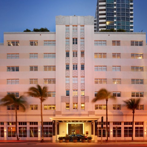 the exterior of a white building with tall palm trees in front at dusk