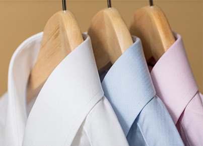 Three different colored dress shirts hanging on wooden hangers