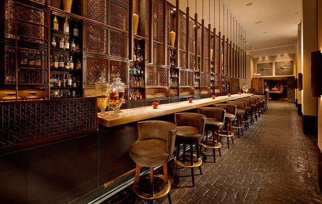 a low lit bar with brown bar stools and large jars of liquid sitting on top of it