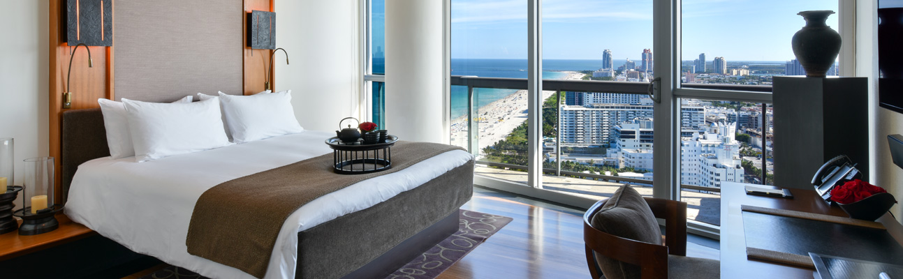 a large bed in a room that has a view of the beach and nearby highrises
