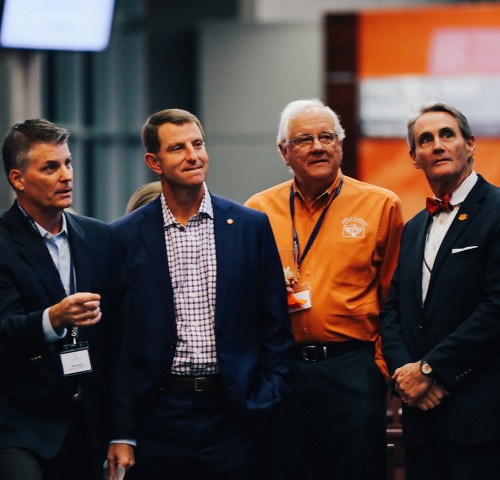 4 men looking at person on stage