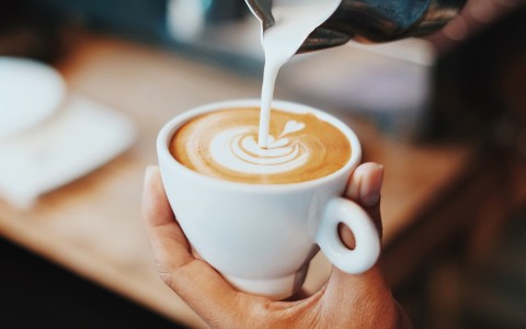 person serving milk in a cup of coffee