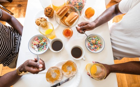 two people eating a bowl of cereal with orange juice, cups of coffee and some bread