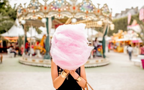 woman holding a piece of cotton candy with carousel in the background