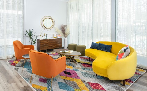 seating area with colorful carpet, coffee table, orange chairs and yellow couch