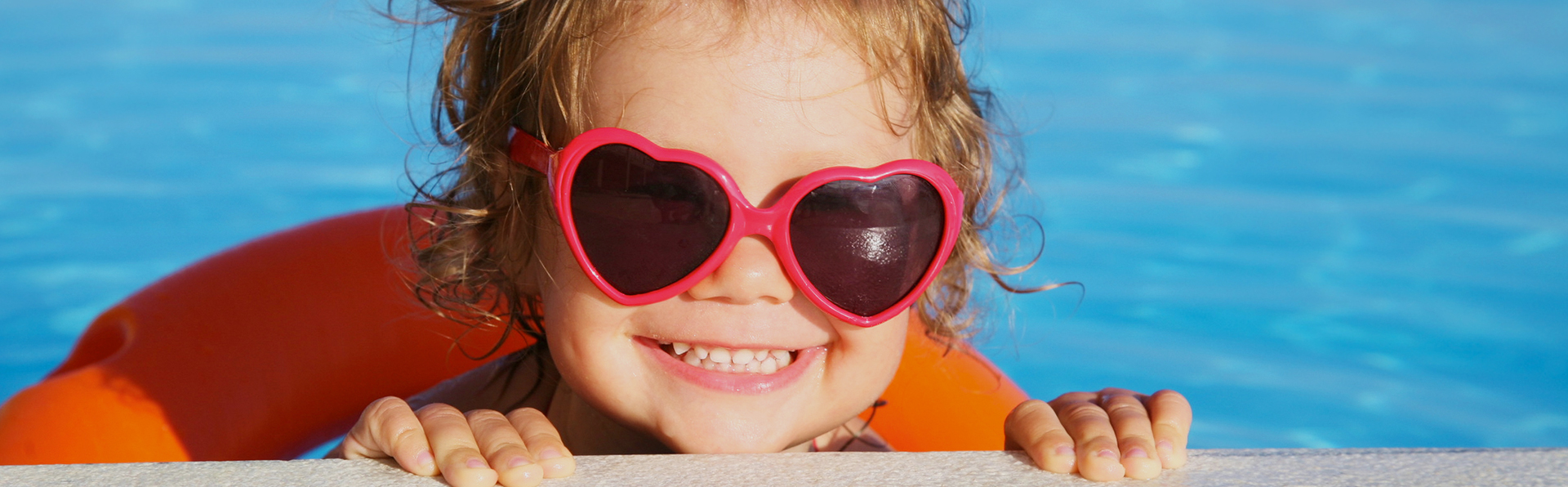 smiling kid with heart sunglasses in the pool 