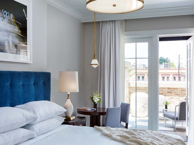corner view of a hotel bedroom with features as a blue headboard two nightstands by the sides and a stylish ceiling light 