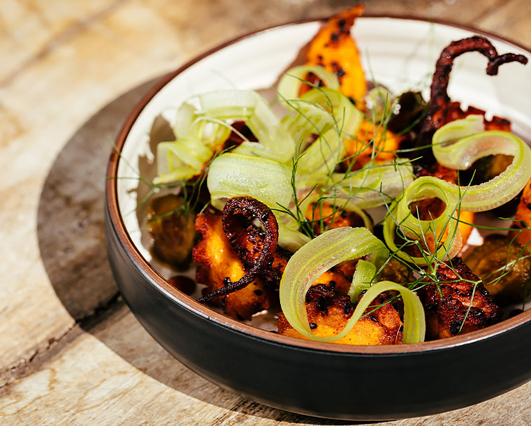 octopus dish with green garnishing in a black bowl