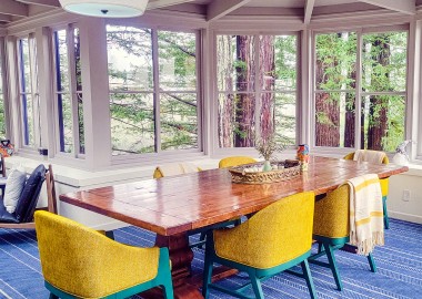 stavrand Sun Room with yellow and teal chairs around table overlooking windows to forest