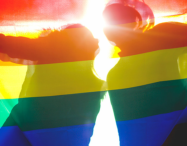 Silhouettes of two people behind rainbow flag