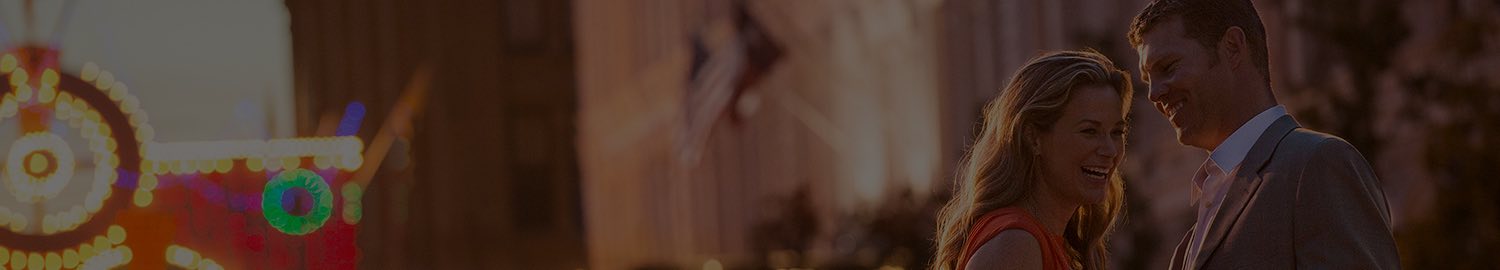 wide header image of couple laughing on pier at nighttime