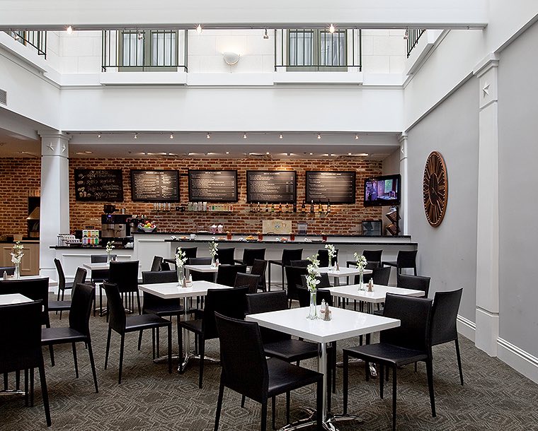 white cafe tables with black chairs and red brick bar in background