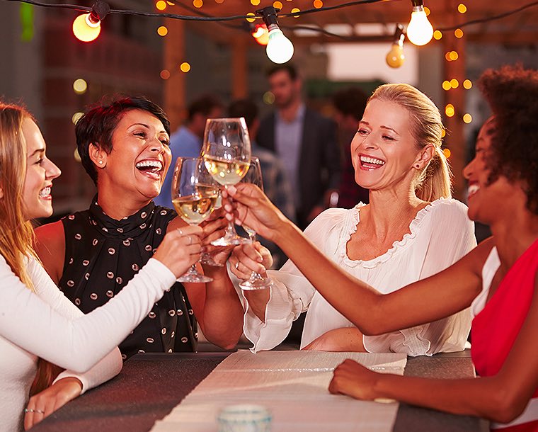 group of women toasting wine glasses under outdoor lights
