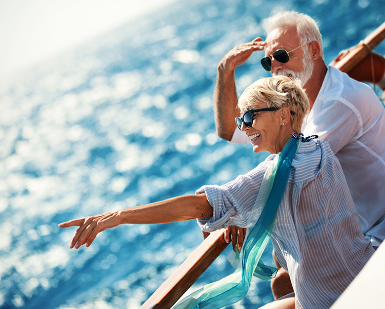 couple on a cruise ship smiling and pointing out to a blue sea