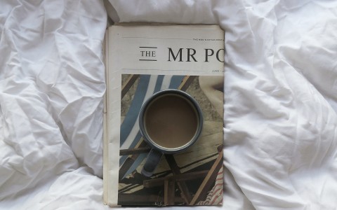 bird eye view of a cup of coffee sitting on top of a newspaper on a bed 