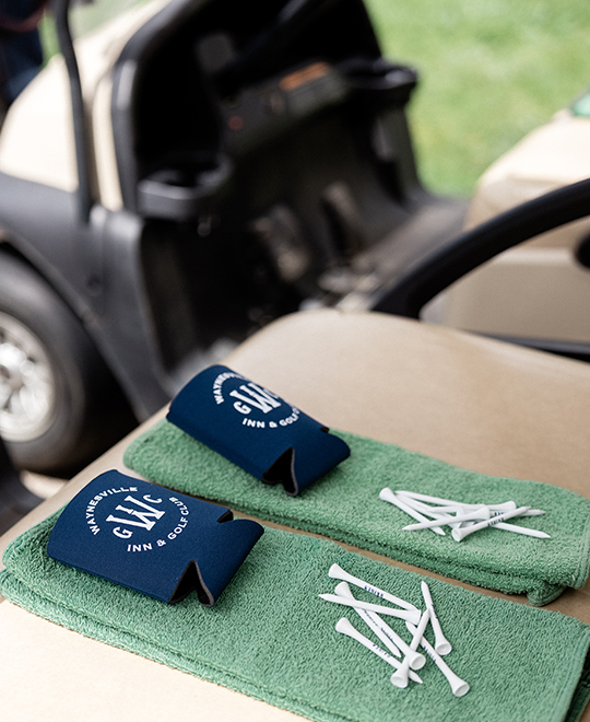 two green golf towels, two koozies, and two piles of golf tees sitting on a golf cart 