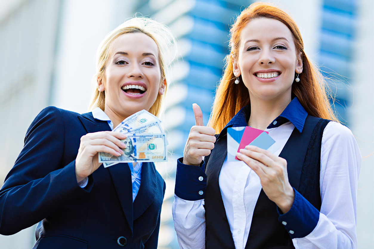 two women smiling holding credit cards and money
