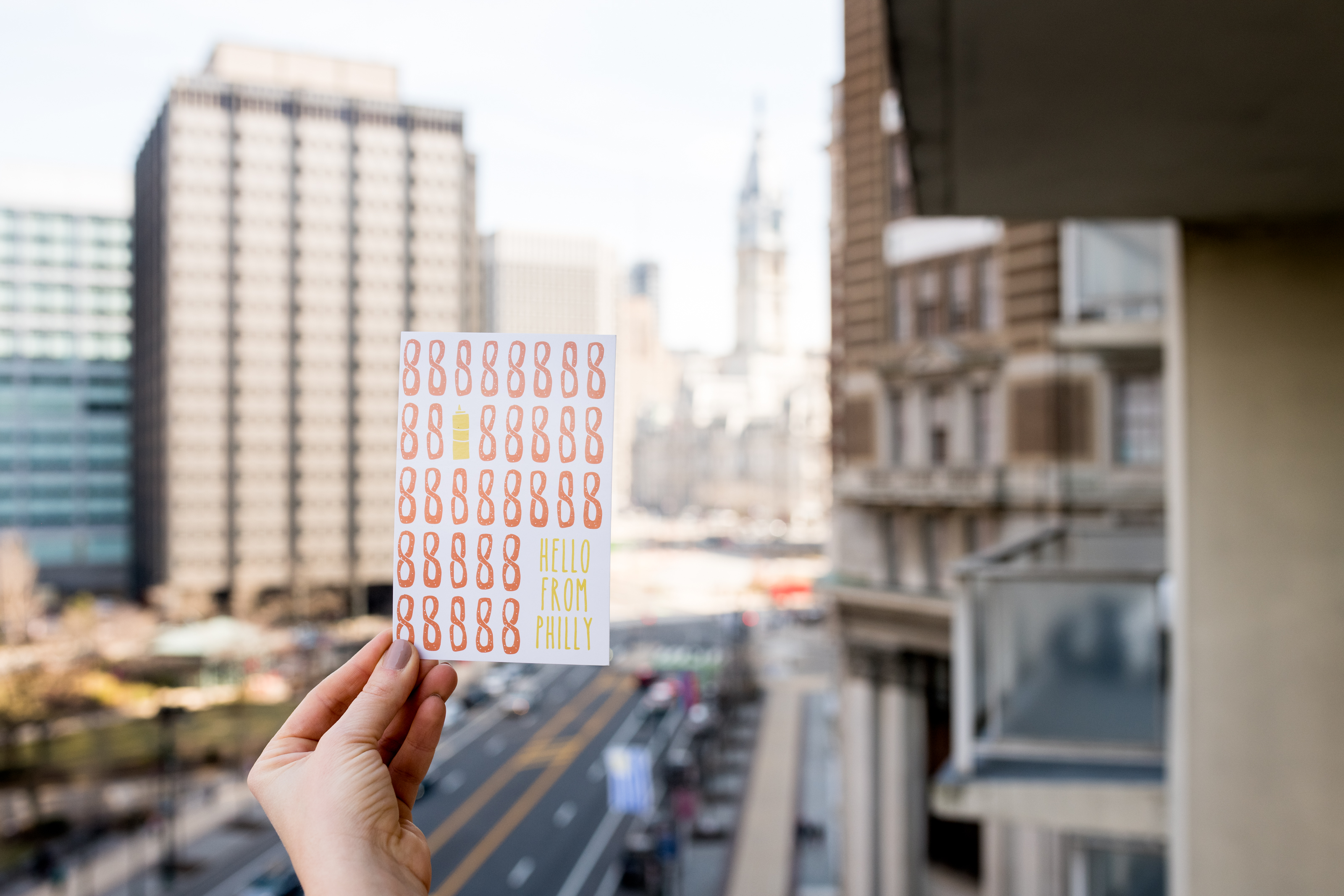 a hand holding a sign in front of a window with buildings in the background