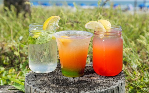 three drinks placed on a tree stomp with the beach in the background